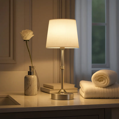 Lamp on a counter with a white rose, books, and towels in a softly lit room.